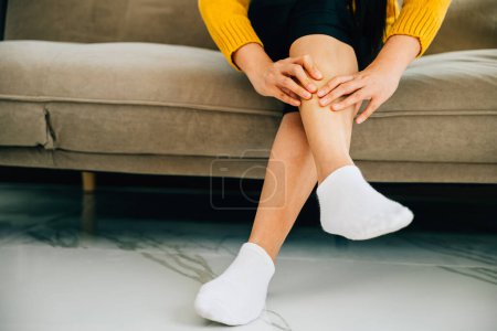 Photo for Close-up of woman on sofa holds her ankle injury feeling pain. Depicting health care varicose vein prevention and emphasizing leg recovery and pain relief concept. medical - Royalty Free Image