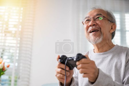 Photo for Asian mature man hands using game controller play videogame, Funny on retirement elderly smile sitting on sofa life gaming, senior old man enjoying holding joystick playing video game at home - Royalty Free Image