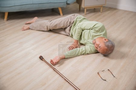 Téléchargez les photos : Asiatique homme âgé tombant couché sur le sol à la maison seul avec bâton de marche en bois dans le salon, Homme âgé maux de tête après la chute, Soins de santé et de la médecine concept - en image libre de droit