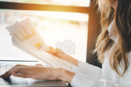Photo for Businesswoman working and comparing forecasting and graphic documents paperwork with laptop computer, Happy female holding papers review report analyzing work results on graph chart outside office - Royalty Free Image