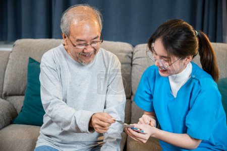 Téléchargez les photos : Un médecin asiatique avec un médecin consulte un patient masculin âgé consulte la posologie de la médecine à la maison dans le salon, une infirmière soignante montrant un médicament sur ordonnance à un homme âgé à la maison de soins infirmiers, un soutien des soins de santé - en image libre de droit