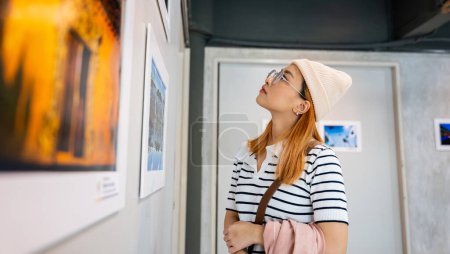 Photo for Woman standing she looking art gallery collection in front framed paintings pictures on white wall, Asian people watch at photo frame to leaning against at show exhibition artwork gallery, Side view - Royalty Free Image
