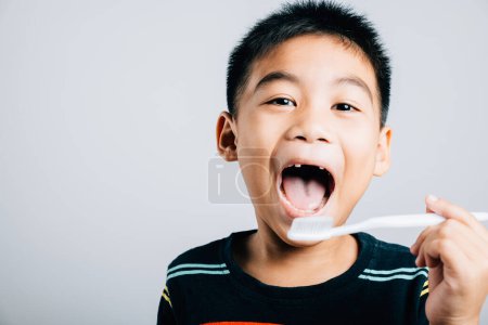 Foto de Aislado sobre un fondo blanco, un niño asiático sin diente de leche superior sostiene un cepillo de dientes que promueve la rutina de higiene dental y la alegría de aprender con una sonrisa alegre. Rutina del dentista infantil - Imagen libre de derechos