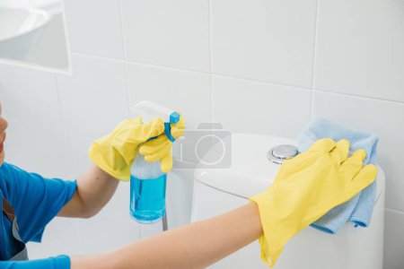 Photo for Diligent woman in rubber gloves scrubs toilet seat with cloth ensuring purity in bathroom cleaning. Her dedication a maid showcases meticulous housekeeping and hygiene. Housekeeper healthcare concept - Royalty Free Image