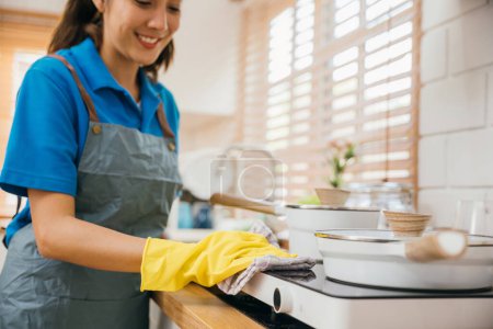 Foto de Mujer asiática mano en guantes de protección limpia el polvo de la estufa de gas en la cocina. Enfatizando la rutina de limpieza de la casa de higiene. Cuidado de la higiene del guante de seguridad de trabajo más limpio. Limpieza de limpieza concepto de limpieza. - Imagen libre de derechos