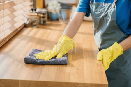 Photo for Housewife or maid in modern kitchen wipes dining table surface. Using professional cleaning products for home tidiness. Cleaner at work safety glove hygiene routine. Maid housekeeping concept. - Royalty Free Image