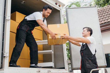 Photo for Smiling employees of a removal company work in uniform unloading boxes and furniture from the truck. Their dedication guarantees a smooth delivery into the new home ensuring happiness. Moving Day - Royalty Free Image