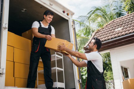 Photo for Moving service workers unload boxes from a truck. Delivery men working together carrying cardboard boxes. Teamwork in relocation. Smiling employees unloading. moving service teamwork. Moving Day - Royalty Free Image
