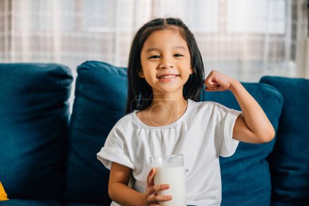 Foto de Un pequeño niño asiático saborea un vaso de leche su comportamiento alegre ejemplificando la importancia del cuidado de la salud y la nutrición en la infancia. - Imagen libre de derechos