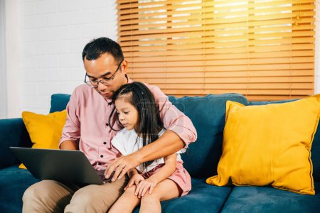 Photo for In a modern living room an Asian businessman combines work with family as his daughter uses a computer for e-learning. Their bonding and happiness showcase the essence of togetherness. - Royalty Free Image
