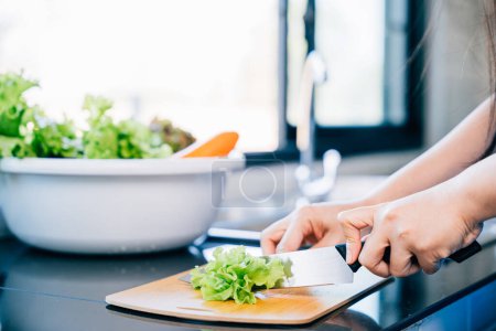 Téléchargez les photos : Une femme dans un tablier bleu coupe des légumes frais pour une salade saine en gros plan. Illustration de la préparation d'ingrédients nutritifs pour un dîner familial à la maison. - en image libre de droit