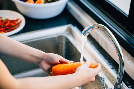 Photo for Hygienic vegetable washing, Young woman carefully washes carrots in the kitchen sink for organic cooking. Emphasizing the importance of cleaning vegetables. - Royalty Free Image