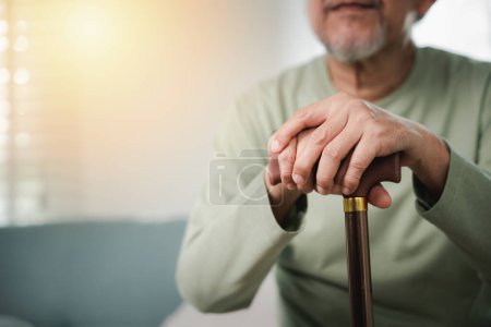 Photo for Closeup hands of senior disabled man holding walking stick, Old man sitting resting on sofa hold wooden walking cane, Elderly hand holding handle of cane, International Day for the Elderly - Royalty Free Image