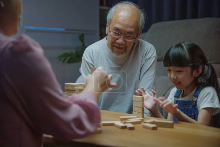 Téléchargez les photos : Heureux grands-parents famille asiatique profiter de jouer bloc jouet avec petite fille et mère ensemble à la maison nuit, souriant parent avoir plaisir à jouer construire tour constructeur de blocs en bois, éducation - en image libre de droit