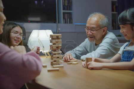 Photo for Happy grandparents Asian family enjoy playing toy block with little daughter and mother together at home night time, Smiling parent having fun play build constructor tower of wooden blocks, education - Royalty Free Image