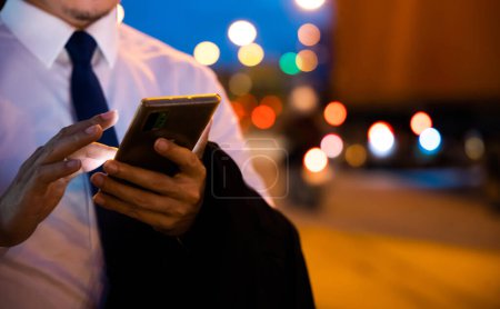 Foto de Young man walking and chatting on mobile phone with friends at social networks outdoor, Portrait Asian businessman typing an sms message via smartphone after work near office at night city street - Imagen libre de derechos