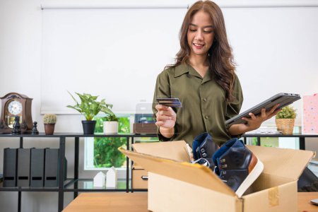 Photo for Asian young woman received online shopping parcel opening shoes boxes to checking on digital tablet, Cheerful woman holding credit card, happy female unpacking cardboard box, Shop online and delivery - Royalty Free Image