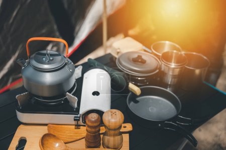 Photo for Enhance your camping adventure, kettle, pot, pan, gas stove, flashlight, and camera neatly set on a table by the tent. The perfect outdoor setup for a memorable journey. - Royalty Free Image