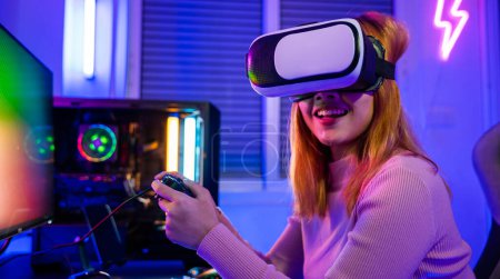 Téléchargez les photos : Femme excitée jouant virtuel manette de jeu elle célèbre la victoire à la maison, Gamer en VR lunettes casque explorer métaverse jouer à un jeu vidéo en ligne avec joystick sur les néons de l'ordinateur - en image libre de droit