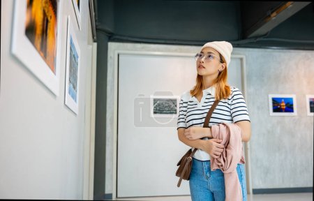 Photo for Asian woman standing she looking art gallery in front of colorful framed paintings pictures on white wall, people watch at photo frame to leaning against at show exhibition artwork gallery, Side view - Royalty Free Image