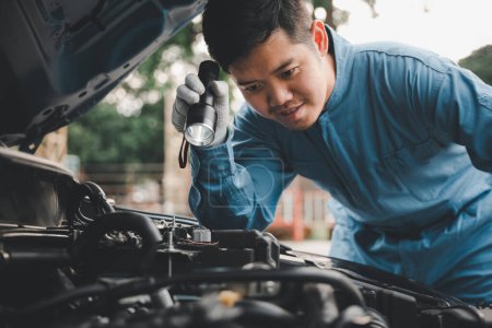 Photo for Young repairman analyzing car problems with an electric lamp on the road. Expert car mechanic repairer checking and repairing auto engine. - Royalty Free Image