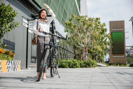Photo for A fashionable biker in the city embraces hot summer season using her hand to shield from sun. Her cheerful smile adds a touch of beauty to bright urban environment. where travel meets happiness. - Royalty Free Image