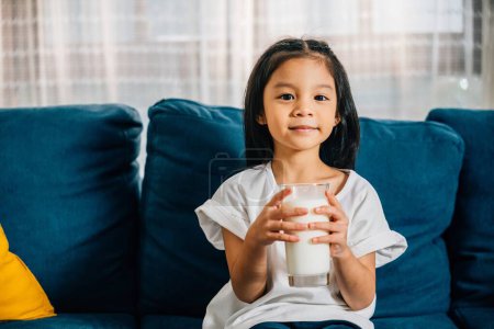 Téléchargez les photos : Gros plan d'un garçon asiatique heureux buvant un verre de lait avec un sourire sur le visage soulignant le rôle d'aliments et de boissons sains dans la vie des enfants. - en image libre de droit