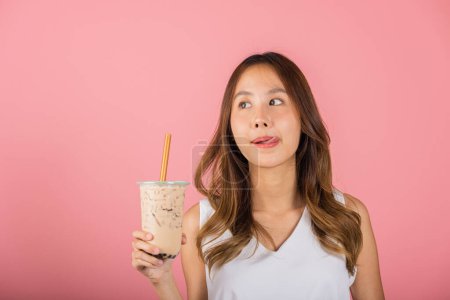 Téléchargez les photos : Asian woman holding drinking brown sugar flavored tapioca pearl bubble milk tea lick lips wanna taste have delighted summer holiday dream, smile female, isolated on pink background, beverage concept - en image libre de droit