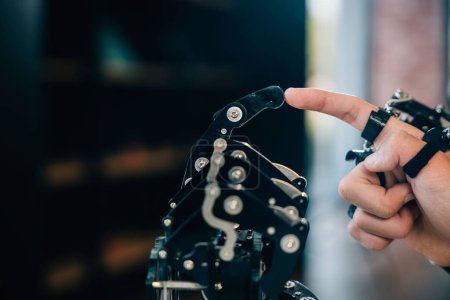 Téléchargez les photos : Dans un collège technique, un adolescent asiatique enthousiaste teste un robot main et bras embrassant la technologie pour le développement éducatif. Explorer l'IA et l'humanité dans des études futuristes. - en image libre de droit