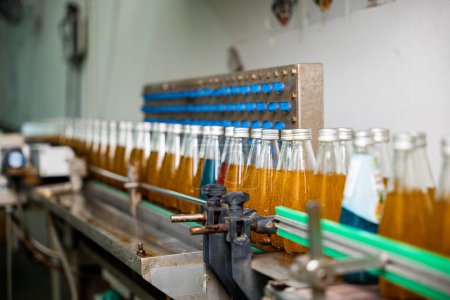 Photo for Transparent bottles move along a conveyor belt in the beverage factory filling up with organic basil seed drinks mixed with pomegranate. This clean automated manufacturing guarantees quality. - Royalty Free Image