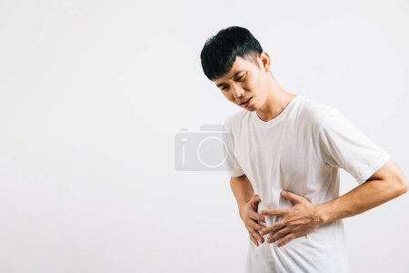 Portrait d'un jeune homme asiatique souffrant de maux d'estomac et de douleurs abdominales, souffrant de problèmes digestifs. Studio tourné isolé sur fond blanc, illustrant des problèmes de santé et de santé.