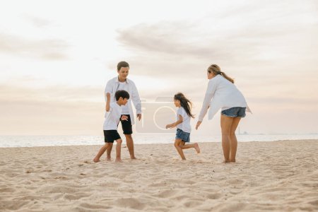 Téléchargez les photos : Joyeux famille sur la plage parents et enfants marchant en jouant et en riant. Vacances d'été bonheur moments insouciants et plaisir en famille au soleil. Temps de qualité rempli de sourires et de joie. - en image libre de droit