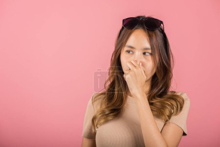 Téléchargez les photos : Asiatique belle jeune femme malheureuse quelle odeur expression dégoûtante serrant le nez avec les doigts. Femme ont quelque chose qui pue mauvaise odeur situation, studio tourné isolé sur fond rose, Soins de santé - en image libre de droit