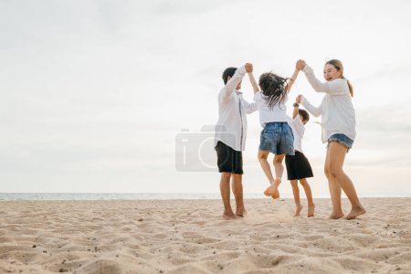 Foto de Una ráfaga de alegría en la playa mientras un padre y una madre de familia asiáticos sostienen a los niños salta al aire. hermoso océano proporciona un entorno sereno para esta deliciosa representación de la unión familiar. - Imagen libre de derechos