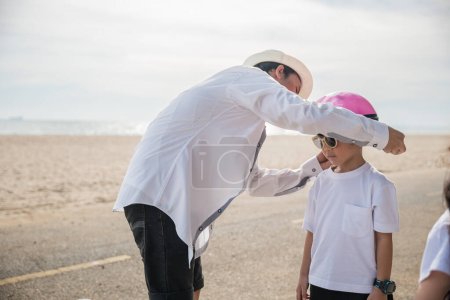 Photo for A family on vacation at the beach where the father sporting a safety helmet teaches his cheerful son the balance and joy of bicycle riding a memorable tourism day filled with family happiness. - Royalty Free Image