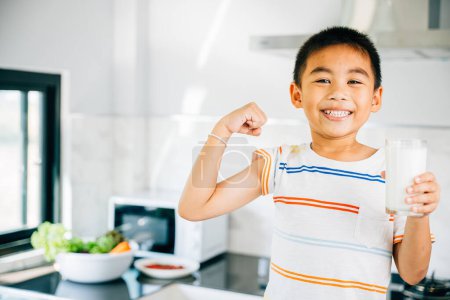 Photo for Adorable Asian little boy holds milk in kitchen, smiling. Portrait of preschool son enjoying drink. Happy child sips calcium-rich liquid, radiating joy at home, Daily life health care Medicine food - Royalty Free Image