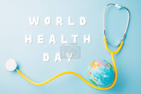 Foto de Día Mundial de la Salud. Estetoscopio médico amarillo y globo terráqueo aislado sobre fondo azul, Save world day, Tierra Verde, Salud y concepto médico - Imagen libre de derechos