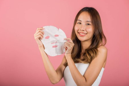 Photo for Healthcare spa. Asian woman holding purifying mask face on hands, Portrait beautiful female smiling holds facial sheet mask, Studio shot isolated on blue background, Face care and beauty treatments - Royalty Free Image