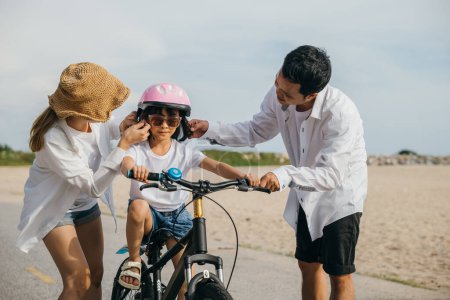 Photo for A memorable summer day on sandy beach as parents teach their children joy of bicycle riding. Smiles safety helmets and freedom of cycling make this delightful family moment filled with carefree fun. - Royalty Free Image