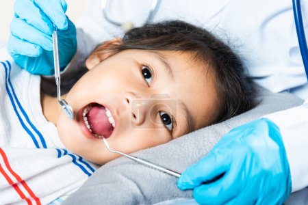Photo for Dental kid health examination. Doctor examines oral cavity of little child uses mouth mirror to checking teeth cavity, Asian dentist making examination procedure for smiling cute little girl - Royalty Free Image
