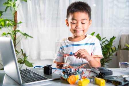 Photo for Asian kid boy assembling board into Arduino robot car homework, Little child assemble DC to DC converter into car toy, creating electronic AI technology workshop online school lesson - Royalty Free Image
