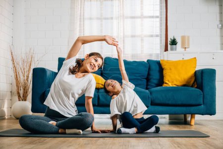 Téléchargez les photos : Une mère asiatique enseigne le yoga à sa fille en se concentrant sur la posture et l'équilibre. Leurs sourires reflètent un heureux moment de famille rempli de vitalité et de détente à la maison. - en image libre de droit