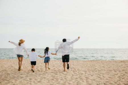 Foto de Una escena familiar alentadora en la playa padres tomados de la mano corriendo y saltando con sus hijos en la risa de vacaciones. Ilustrando la felicidad y la unión de unas vacaciones sin preocupaciones en la playa. - Imagen libre de derechos