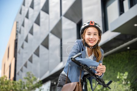 Foto de Un viaje de negocios asiático por la mañana es un retrato de alegría. Ella está de pie con su casco de bicicleta y se adaptó encarnando el concepto moderno de un alegre viajero de negocios. - Imagen libre de derechos