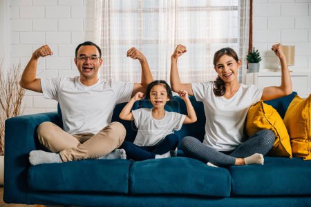 Photo for In their cozy living room at home young parents mom and dad join their child and daughter in showcasing biceps muscles symbolizing family strength and togetherness on this special Family Day. - Royalty Free Image