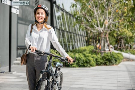 Photo for Asian businesswoman morning commute is portrait of cheerfulness. She stands by her bicycle helmeted and suited up embodying modern concept of business commuter where work and outdoor fun coexist. - Royalty Free Image