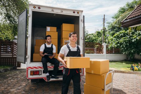 Photo for Delivery men unload boxes from a truck. Movers in uniform cooperate in a relocation service. Teamwork and cooperation among colleagues. Smiling workers carrying boxes. relocation teamwork Moving Day - Royalty Free Image