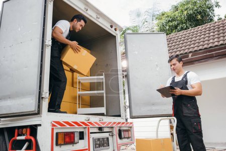 Photo for Uniformed removal company workers unload boxes and furniture from the truck exhibiting excellent teamwork. Their dedication guarantees a smooth move into the new home ensuring happiness. Moving Day - Royalty Free Image