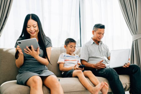 Photo for Parents kids engaged with laptops and phones ignoring familial bonding. An Asian familys device dependence portrays the challenges of internet addiction. ignores togetherness - Royalty Free Image