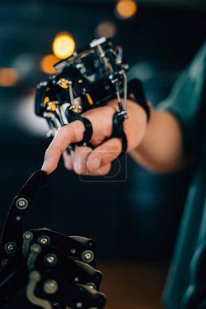 Foto de En una universidad técnica, un adolescente aprende tecnología probando una mano robótica y un brazo tocando los dedos para mejorar sus habilidades educativas. Abrazar la IA futurista y la humanidad. - Imagen libre de derechos